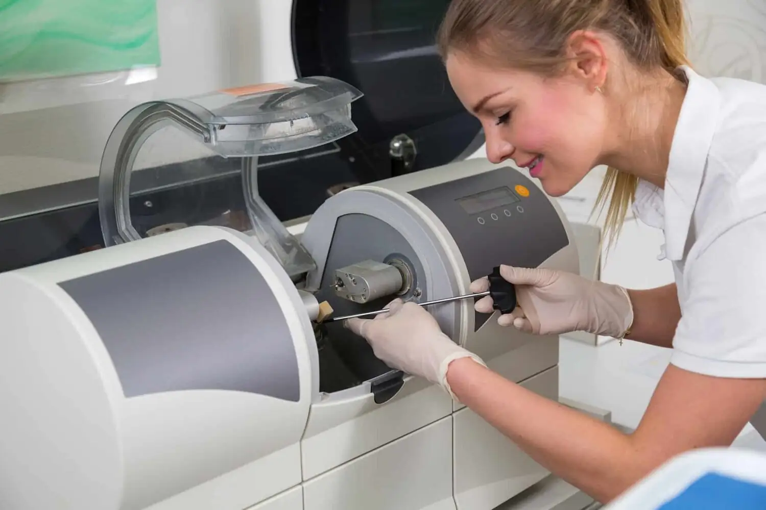 A dental professional using a tool to adjust a dental crown milling machine.