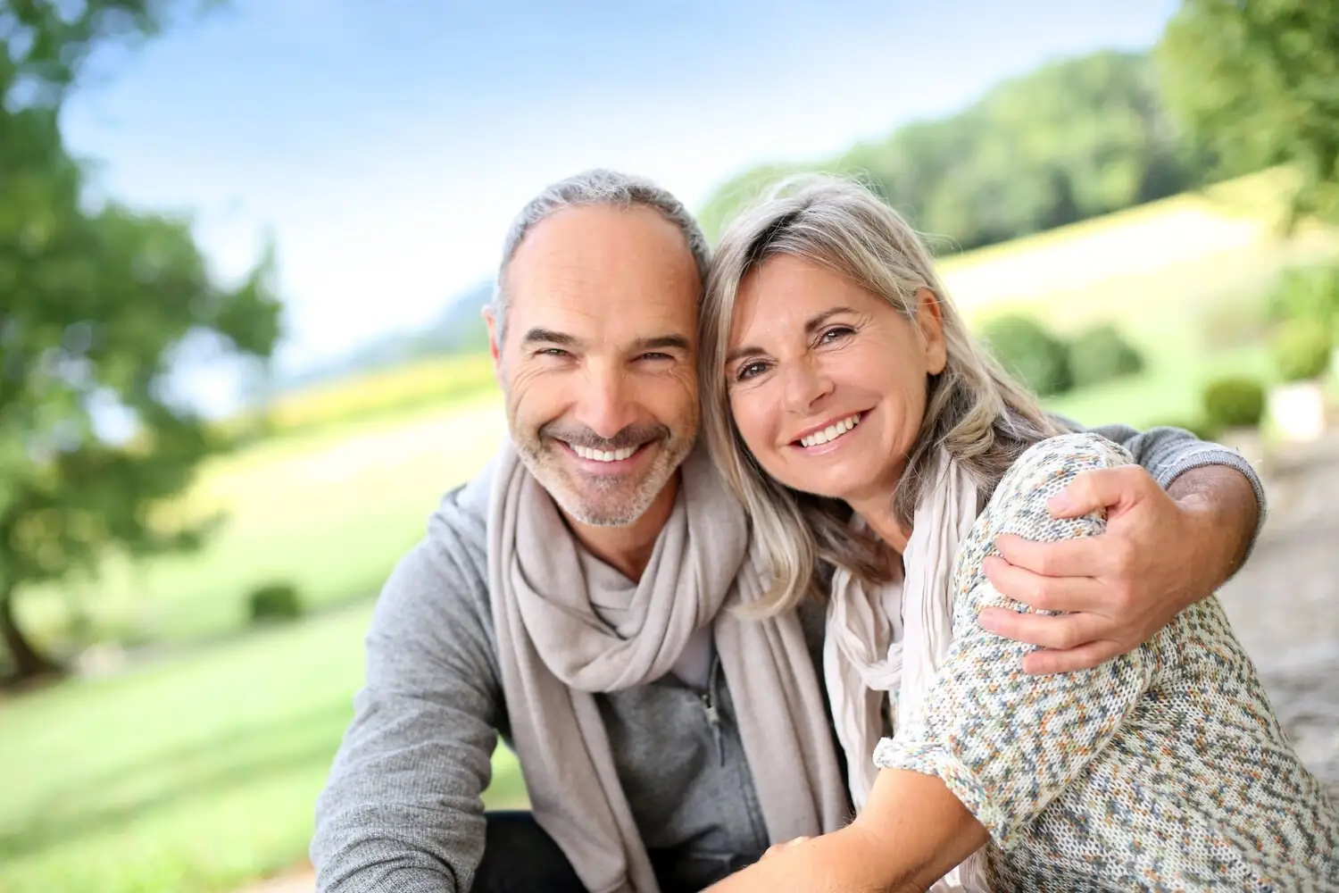 Two adults embracing and smiling outdoors.